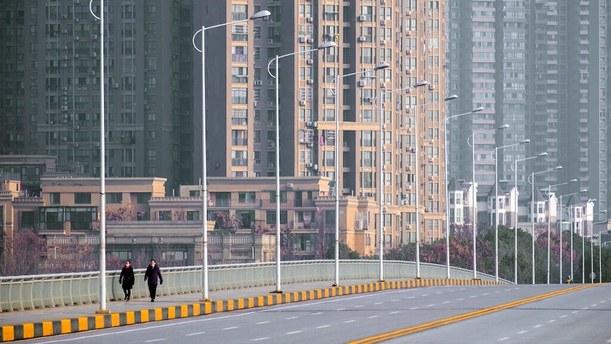 Bạn nhìn thấy một cây cầu sáu làn xe trống trải ngoài hai người đi bộ với những tòa nhà cao tầng mọc lên phía sau họ.